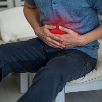 a person in a blue shirt clutches their abdomen which is highlighted with a red light